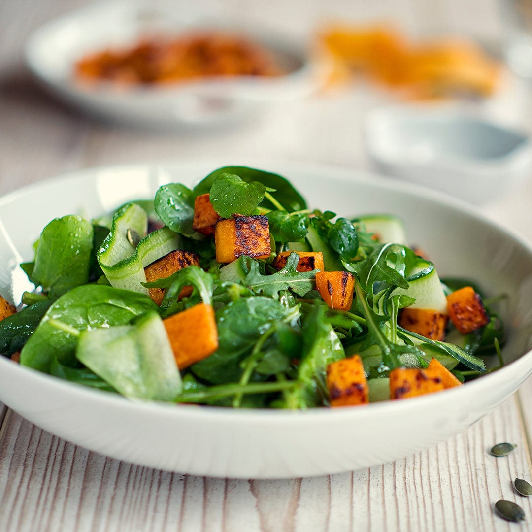 A salad with fresh baby spinach grown from Back to the Roots Organic Spinach Seeds—'Bloomsdale', cucumber, and roasted butternut squash is served in a white bowl on a light wooden table.