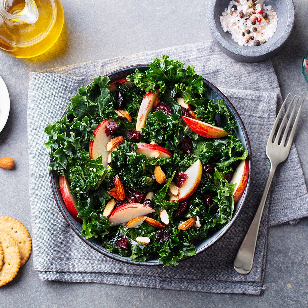 Enjoy a nutritious bowl of greens grown from Back to the Roots Organic Kale Seeds—'Dwarf Blue Curled Vates'—served as kale salad with apples, almonds, and dried cranberries, alongside crackers, olive oil, and seasonings.