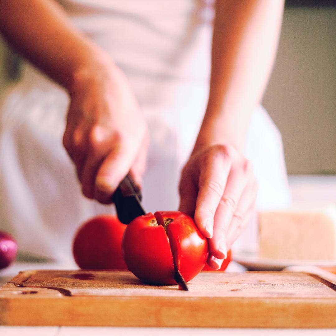 Hand slicing a ripe red Rutgers tomato on a wooden cutting board with a black-handled knife. - Organic Tomato Seeds — 'Rutgers' - Default Title - Back to the Roots