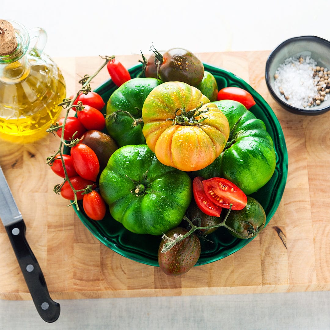 Assorted heirloom tomatoes including green, yellow, red, and striped varieties on a green plate with olive oil and salt on a . - Organic Tomato Seeds — 'Big Rainbow' - Default Title - Back to the Roots