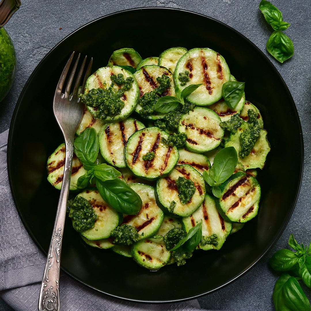 Black grilled zucchini slices topped with green pesto and fresh basil leaves in a black bowl with a silver fork. - Organic Zucchini Seeds — 'Black' - Default Title - Back to the Roots