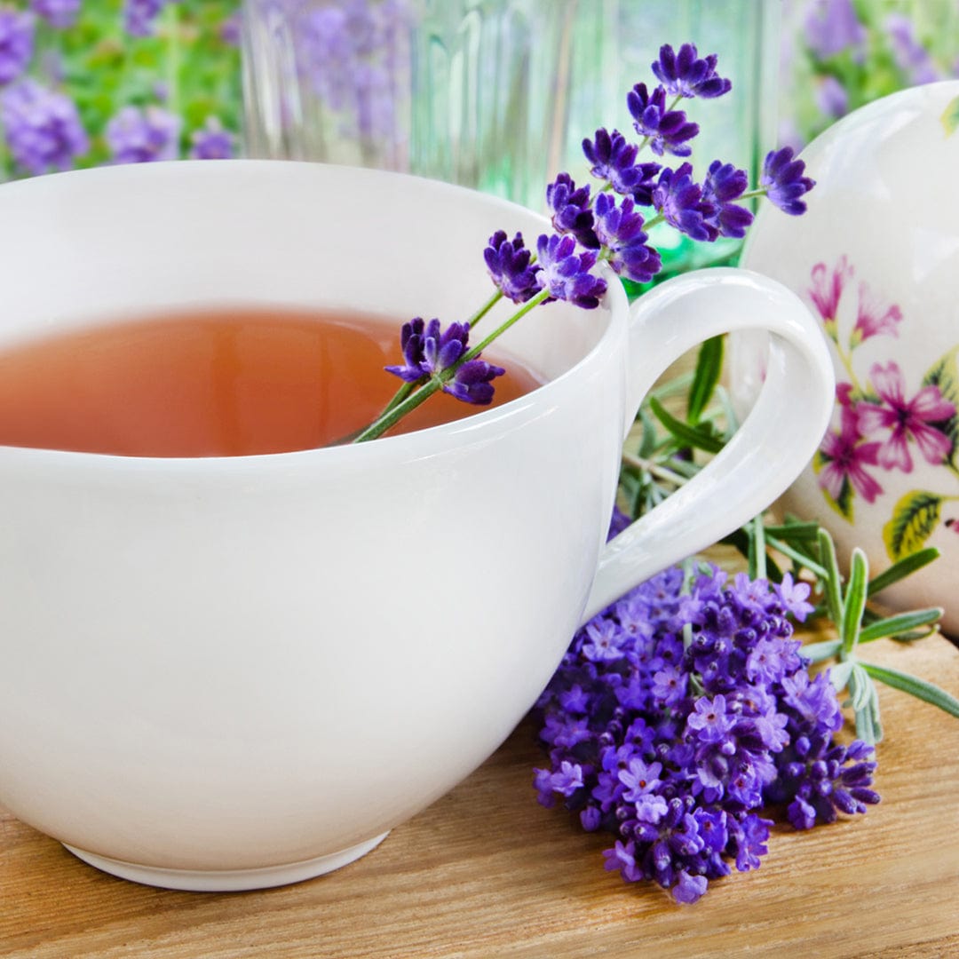 A cup of tea with fragrant lavender and a floral teapot on wood, featuring Back to the Roots Organic Lavender Seeds—‘English’—and a small bunch of this perennial herb.