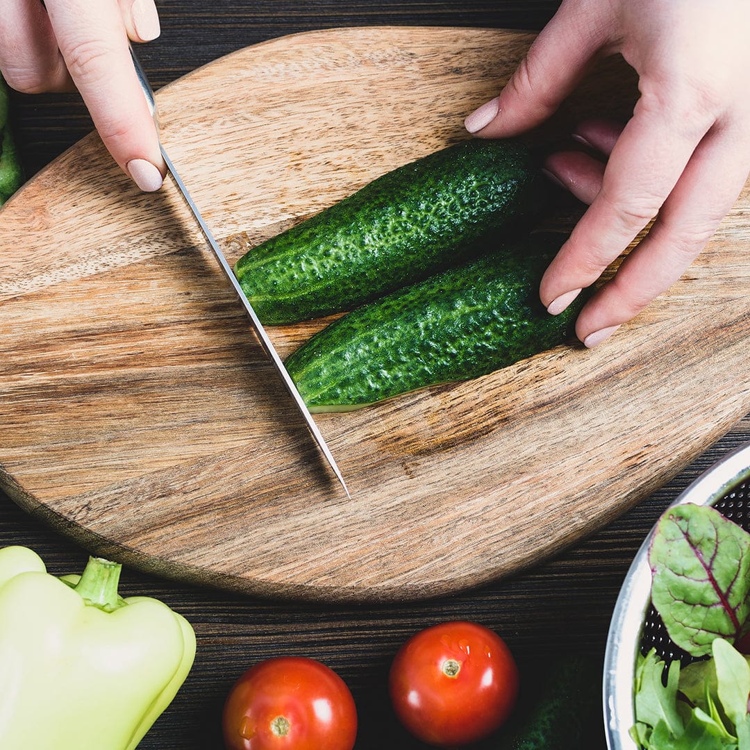 Hands slicing two dark green cucumbers on a wooden cutting board, with tomatoes and greens nearby. - Organic Cucumber Seeds — 'Slicing • Spacemaster' - Default Title - Back to the Roots