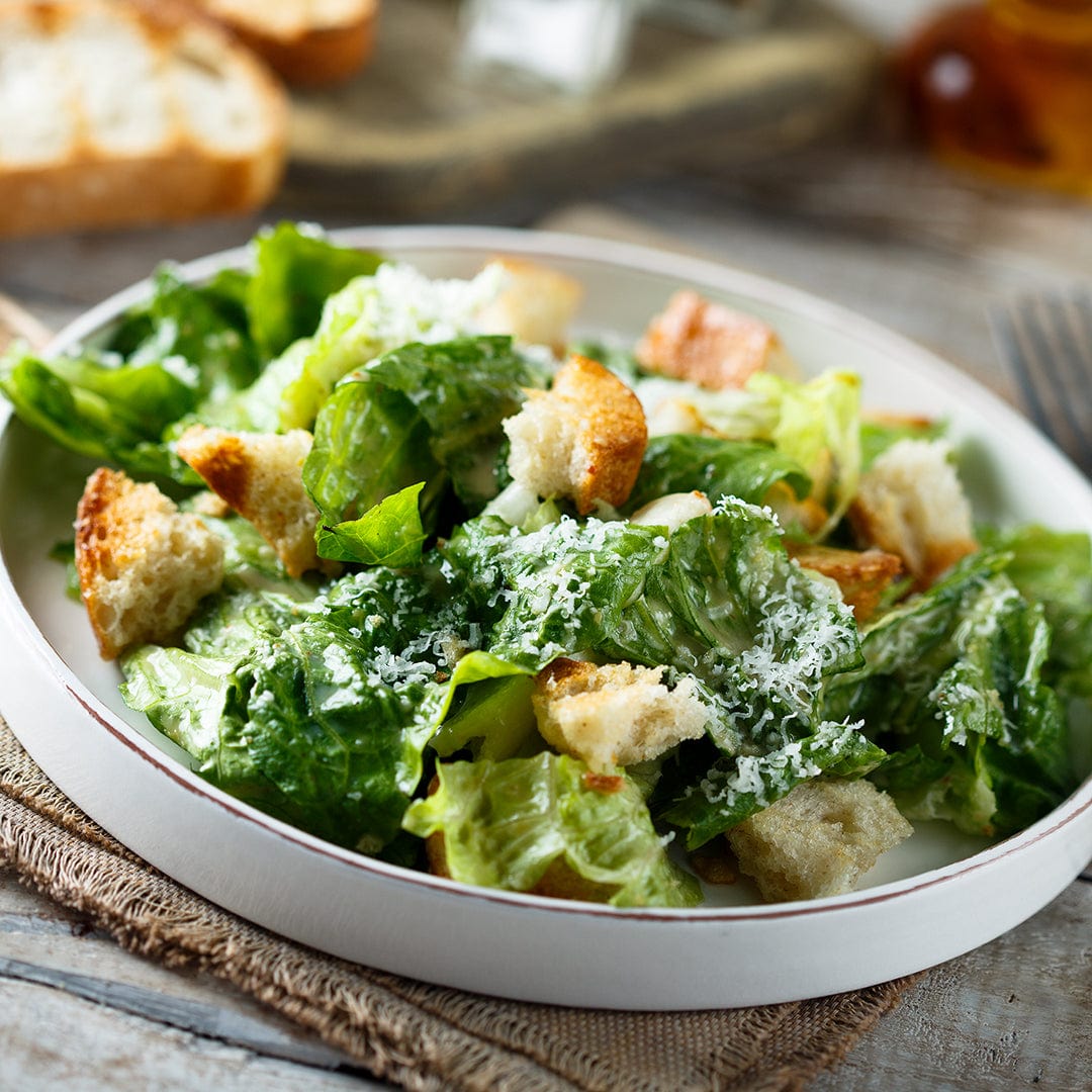 A plate of Caesar salad with crisp romaine grown from Back to the Roots Organic Lettuce Seeds — Romaine 'Paris Isle Cos', topped with croutons and grated cheese, served on a rustic table.