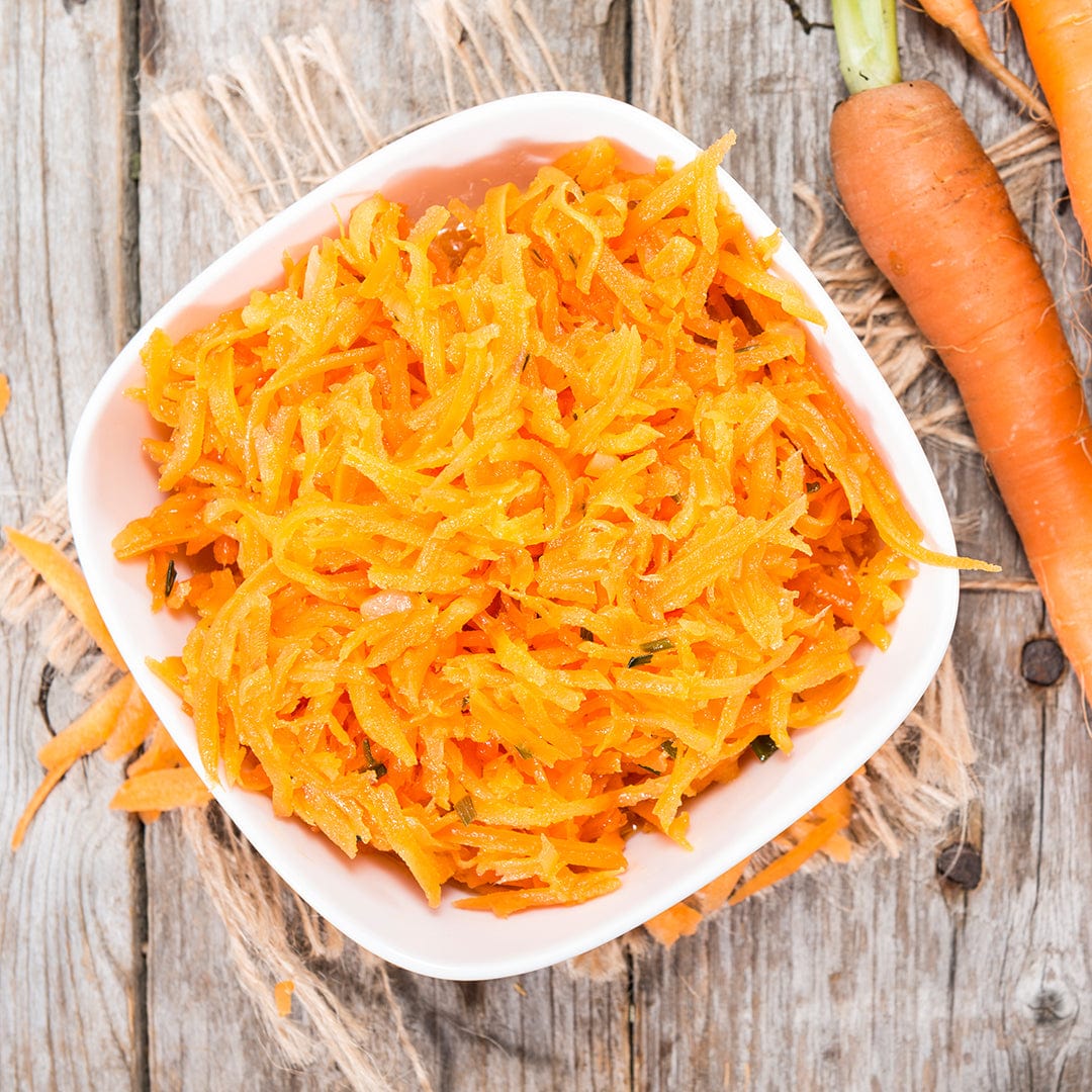 A white bowl of shredded carrots and fresh carrots rests on a rustic wooden surface—perfect inspiration for gardeners to grow their own with Back to the Roots Organic Carrot Seeds, 'Chantenay Red Cored'.