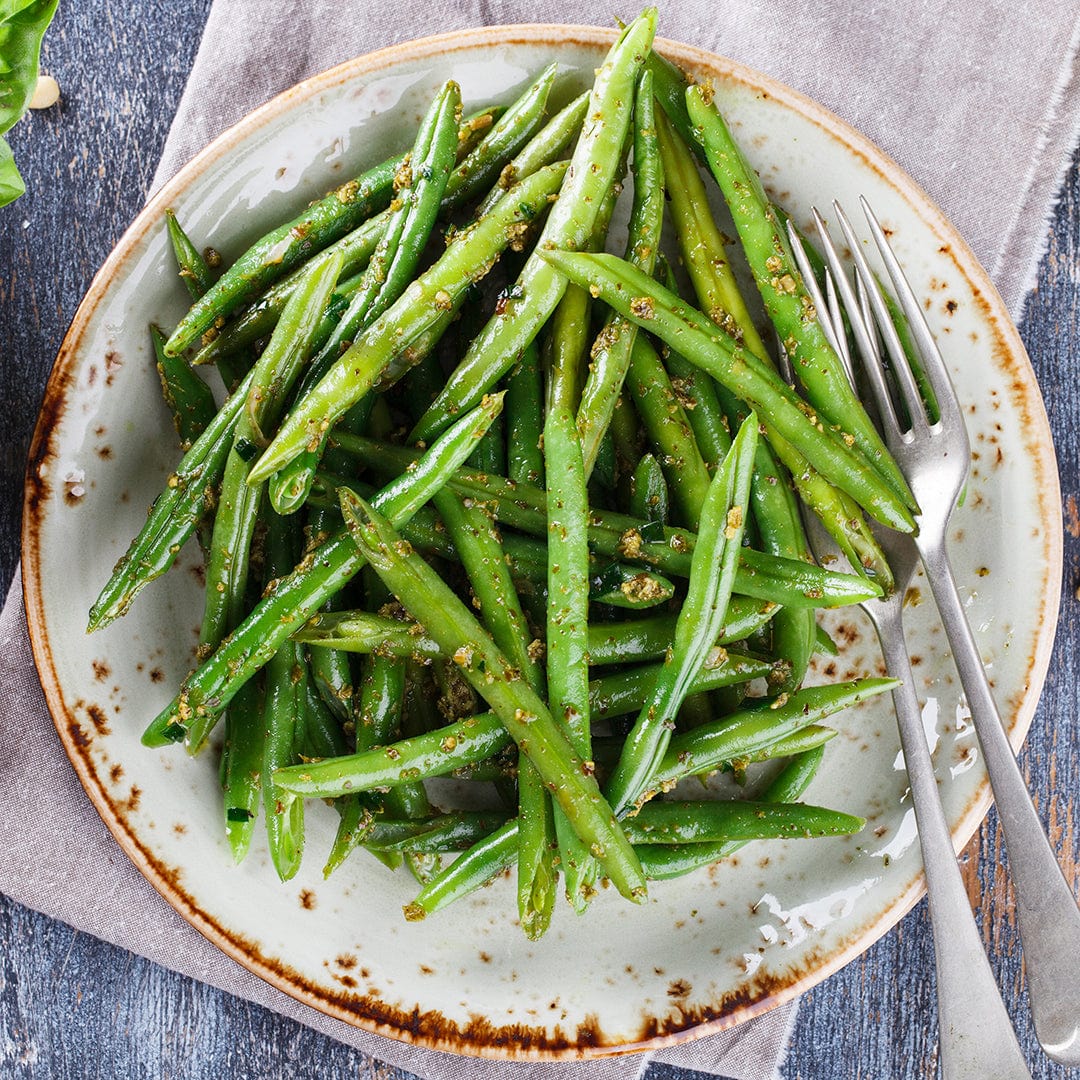 A plate of cooked pole beans made from Back to the Roots Organic Bean Seeds—'Kentucky Wonder Pole Green'—is seasoned with spices and served with a fork on a rustic ceramic plate atop a gray napkin.
