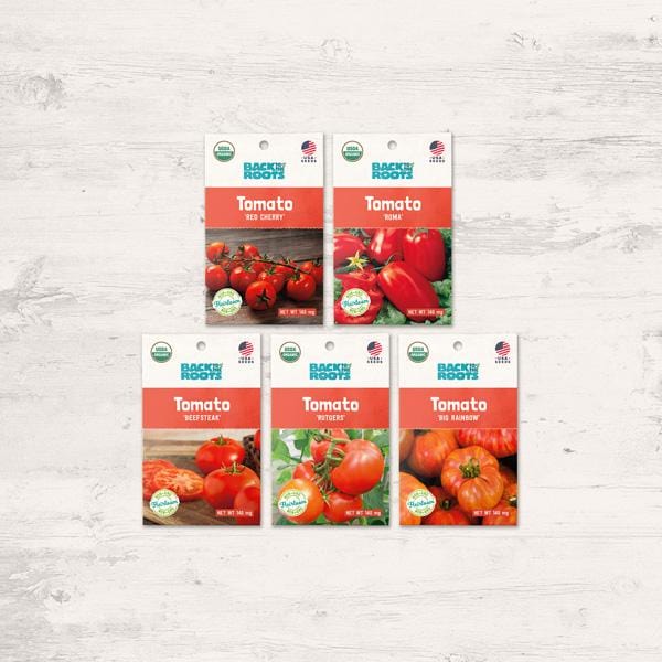 Five packets of the Organic Heirloom Tomato Variety Pack - Seed Packet Bundle by Back to the Roots are displayed on a light wooden surface, each packet highlighting a different vibrant tomato variety.