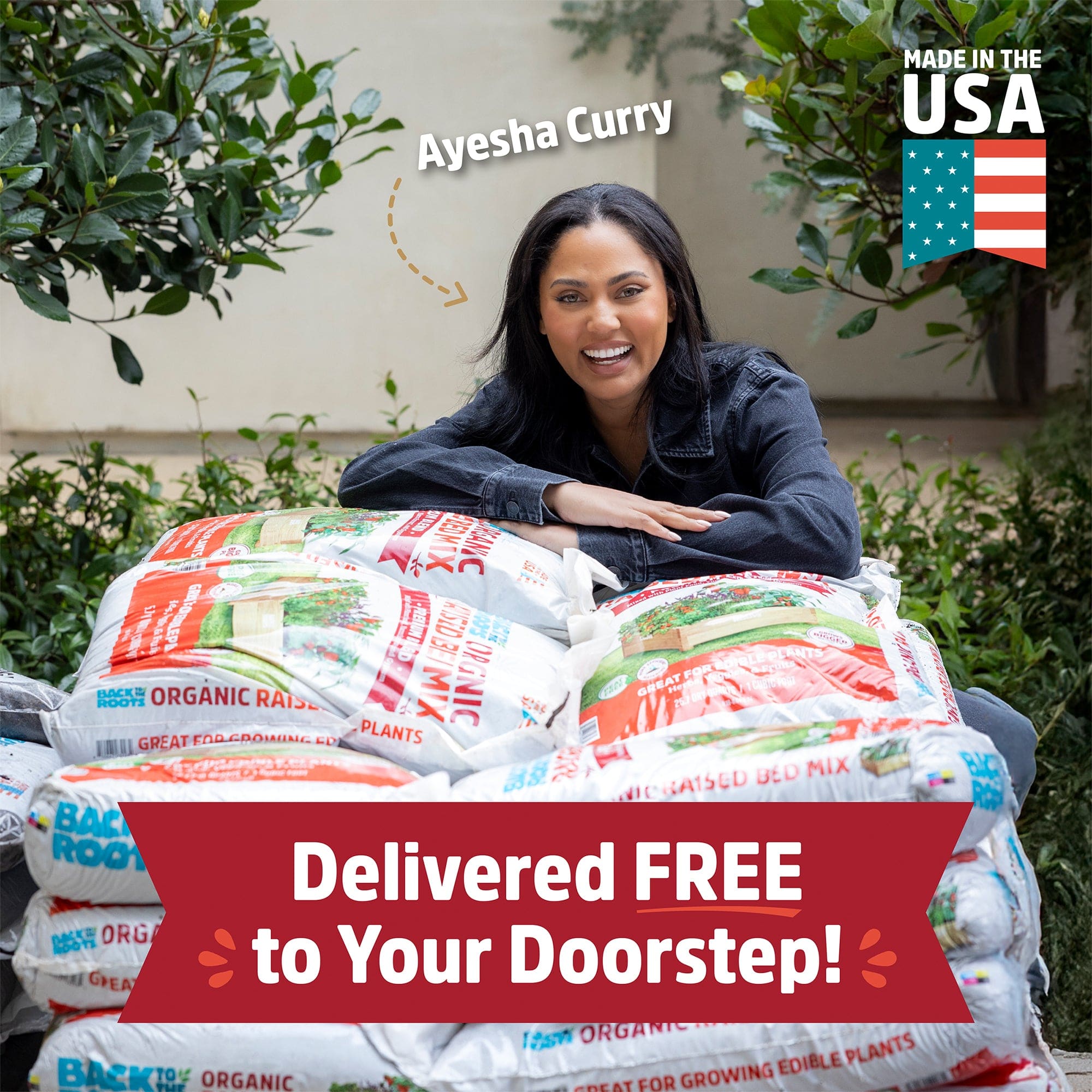 A woman smiles behind several bags of Back to the Roots Organic Raised Bed Mix: Bulk Truckload (44 Cu. Yds, 1200 1CF Bags). Text reads, "Delivered FREE to Your Doorstep!" and "Made in the USA.