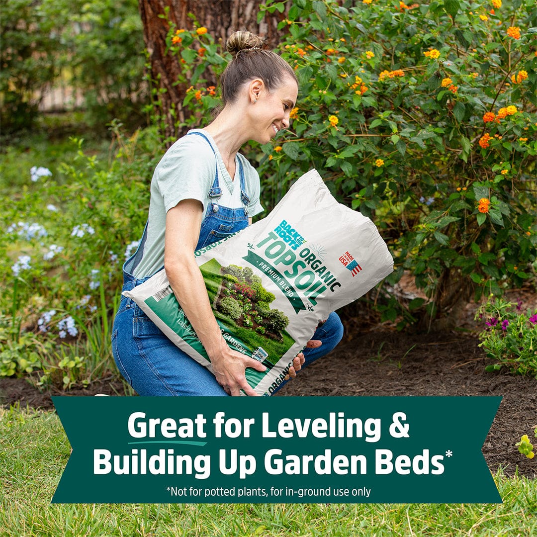 Woman carrying a large white bag of organic bulk topsoil with green and brown labeling, outdoors in garden setting. - Organic Bulk Topsoil (30 1 cu.ft. Bags) - Default Title - Back to the Roots