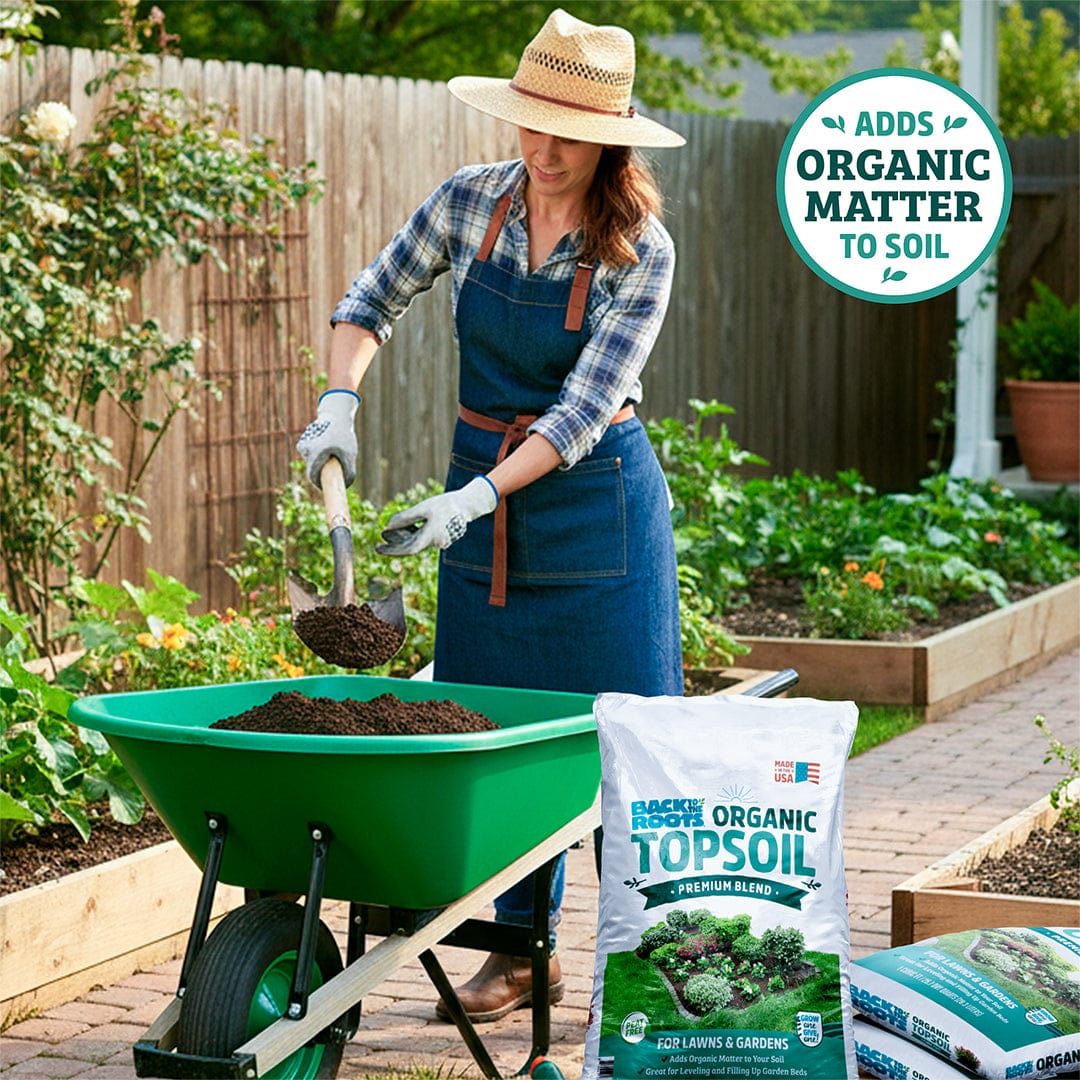 Woman in denim apron and straw hat loading dark, rich organic topsoil from bag into bright green wheelbarrow in garden. - Organic Bulk Topsoil (30 1 cu.ft. Bags) - Default Title - Back to the Roots