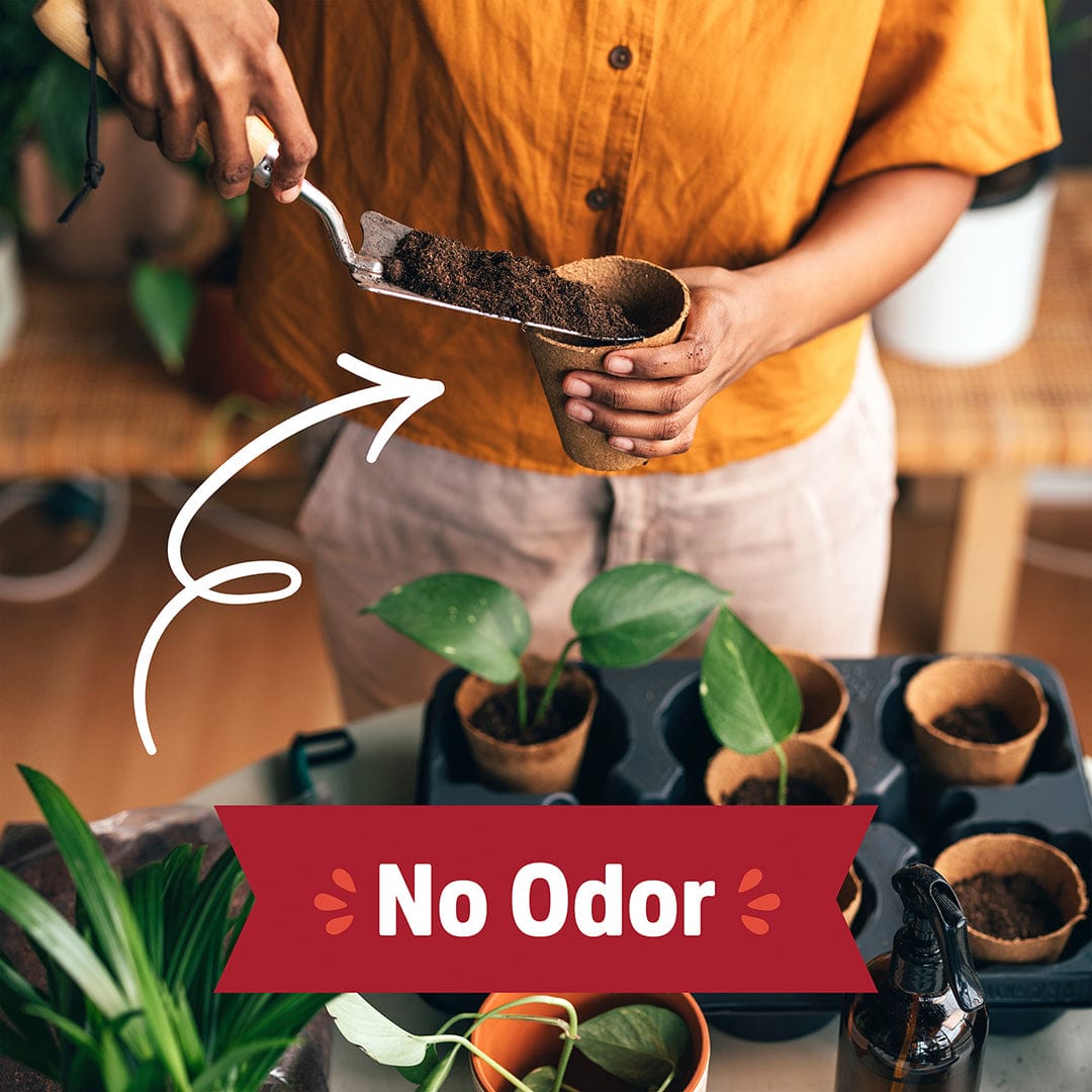 Hands holding a brown pouch filled with dark organic worm castings over small plant pots, wearing a mustard yellow shirt,. - Organic Worm Castings 5lb Pouch - Default Title - Back to the Roots