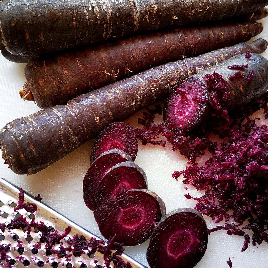 Dark purple elongated carrots whole and sliced, showing vibrant magenta interior with shredded carrot bits nearby. - Organic Carrot Seeds — 'Purple Dragon' - Default Title - Back to the Roots